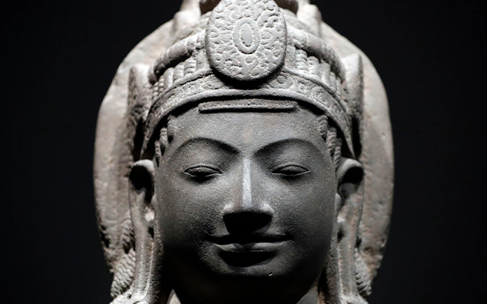 Stone sculpture of a serene face with intricate headdress at Asian Civilisations Museum.
