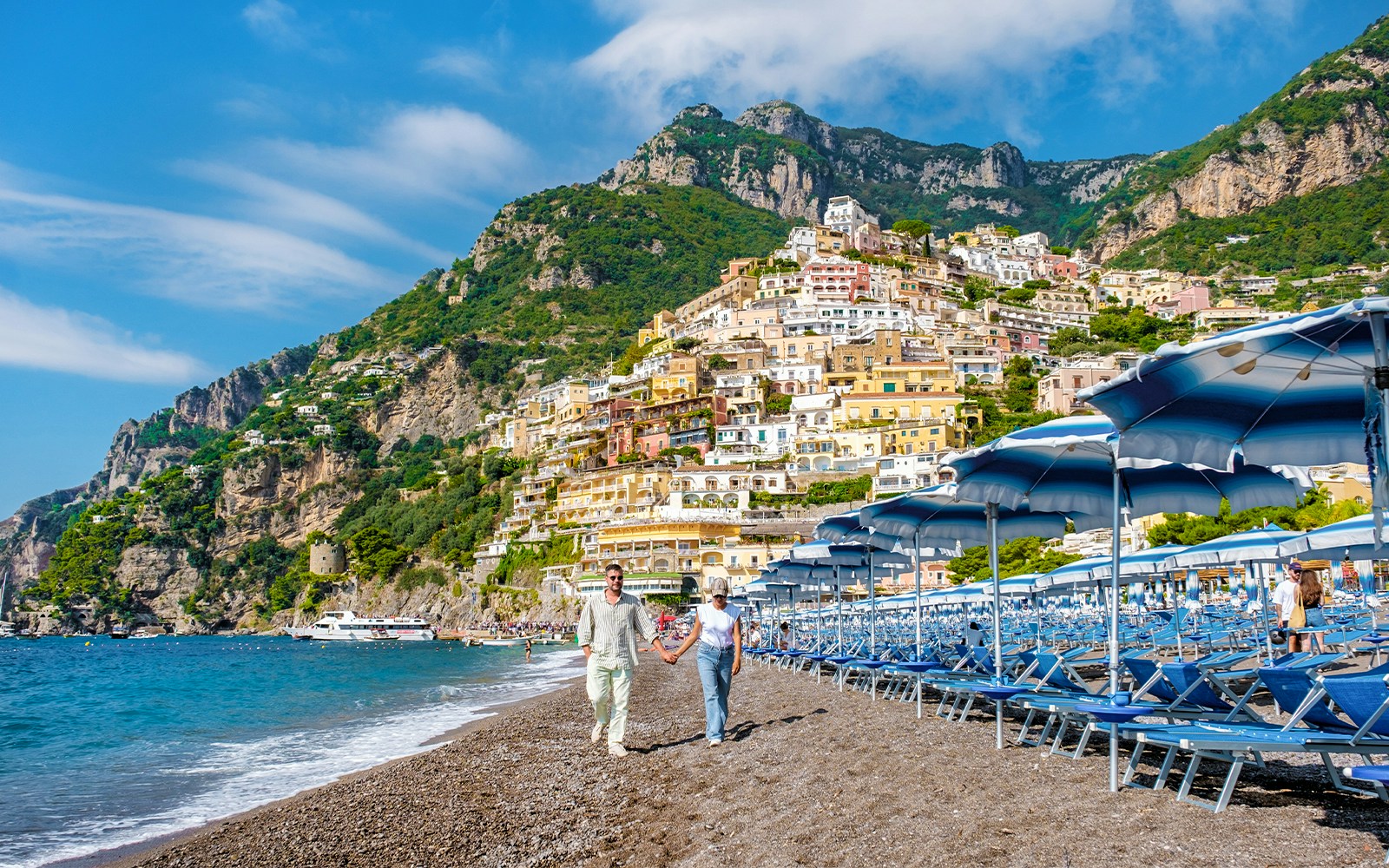 tourists enjoying Walking along the Amalfi coast beach with colorful Positano in the background on a sunny day