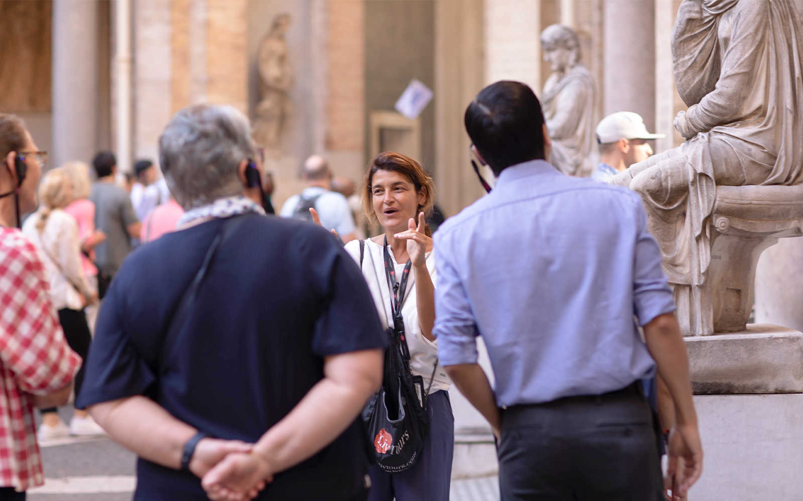 Guide leading a small tour group at the Vatican Museum, standing near classical statues.