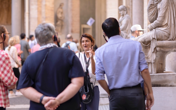 Guide leading a small tour group at the Vatican Museum, standing near classical statues.