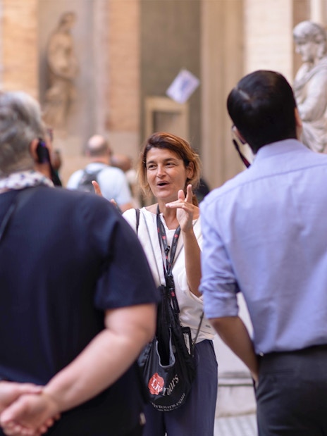 Guide leading a small tour group at the Vatican Museum, standing near classical statues.