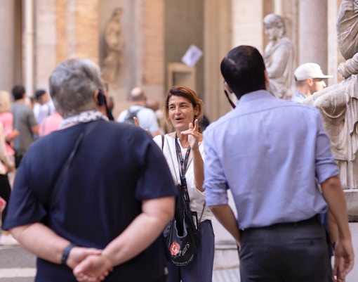 Guide leading a small tour group at the Vatican Museum, standing near classical statues.