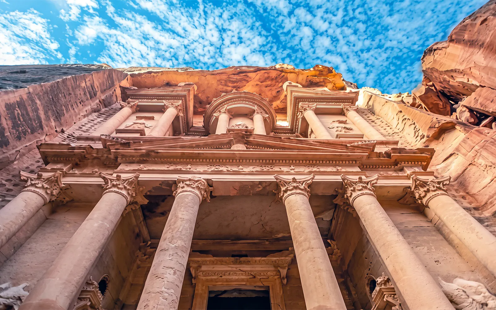 Petra's Al-Khazneh facade with columns under a blue sky, Jordan.