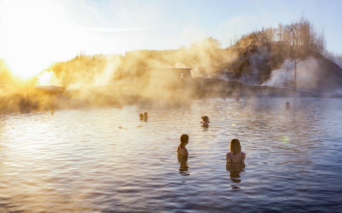 People enjoying the geothermal waters at Secret Lagoon, Gamla Laugin, with steam rising in the background.