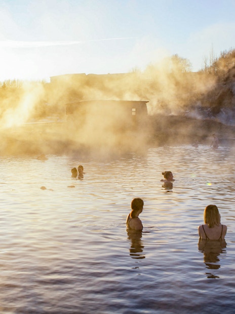 People enjoying the geothermal waters at Secret Lagoon, Gamla Laugin, with steam rising in the background.