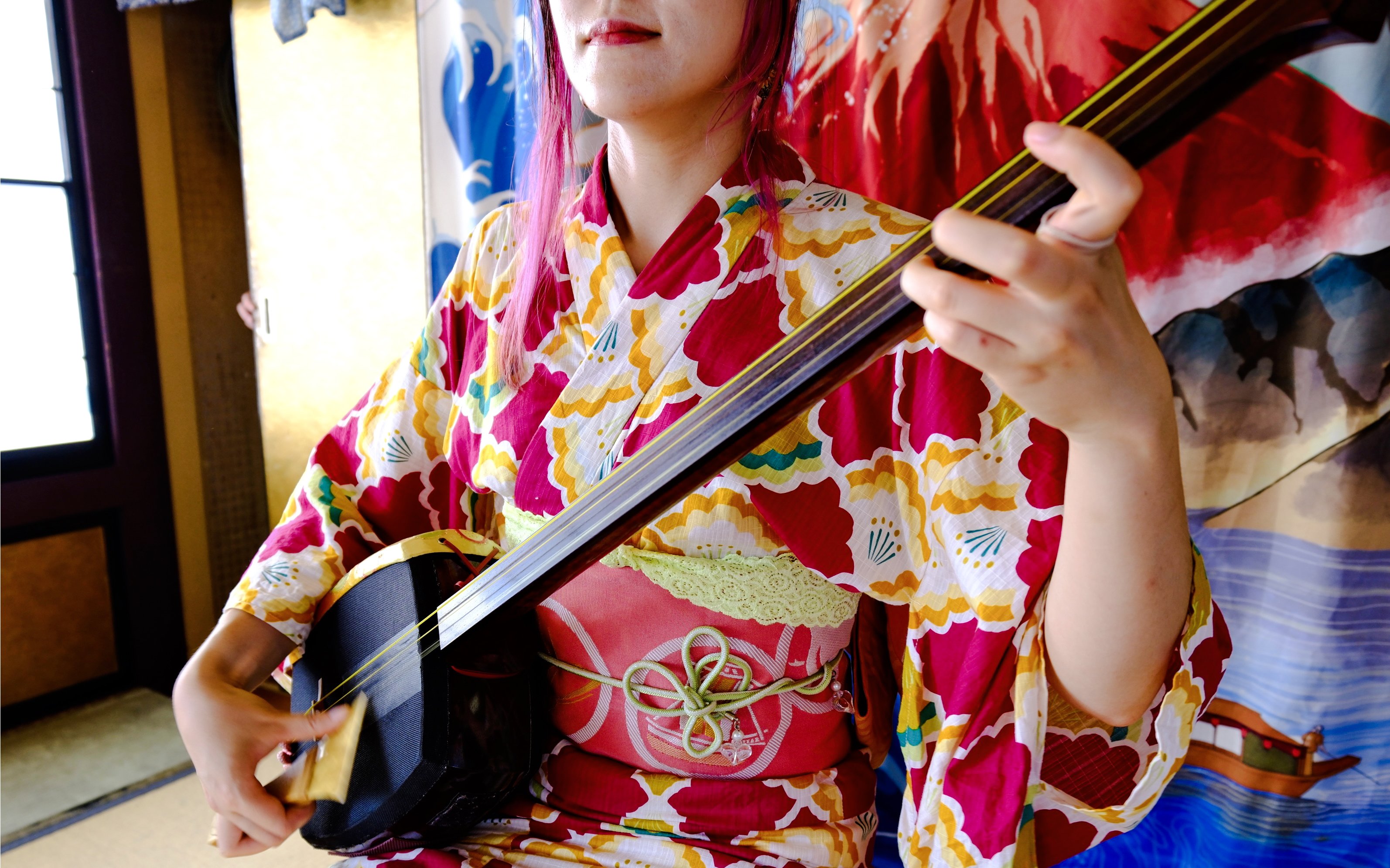 Person playing a shamisen in traditional Japanese attire.