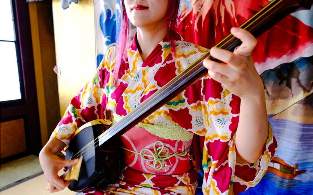Person playing a shamisen in traditional Japanese attire.