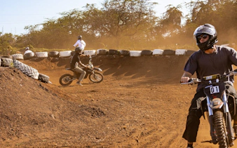 Riders on electric dirt bikes navigating a dirt track in Oahu with expert guidance.