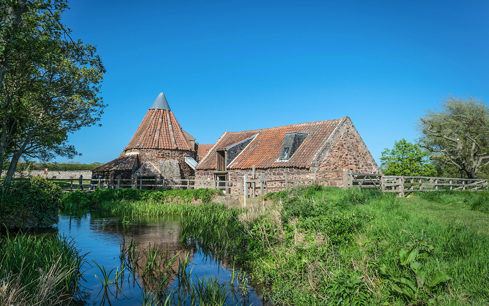 Mill building with red-tiled roof at Hobbiton Movie Set, surrounded by greenery and a stream.