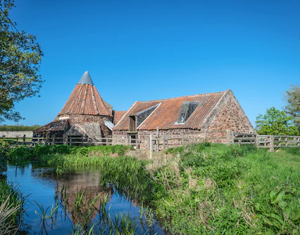 Mill building with red-tiled roof at Hobbiton Movie Set, surrounded by greenery and a stream.