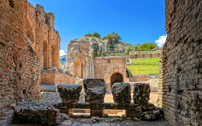 Taormina Ancient Theatre ruins with stone columns and archways, Sicily.