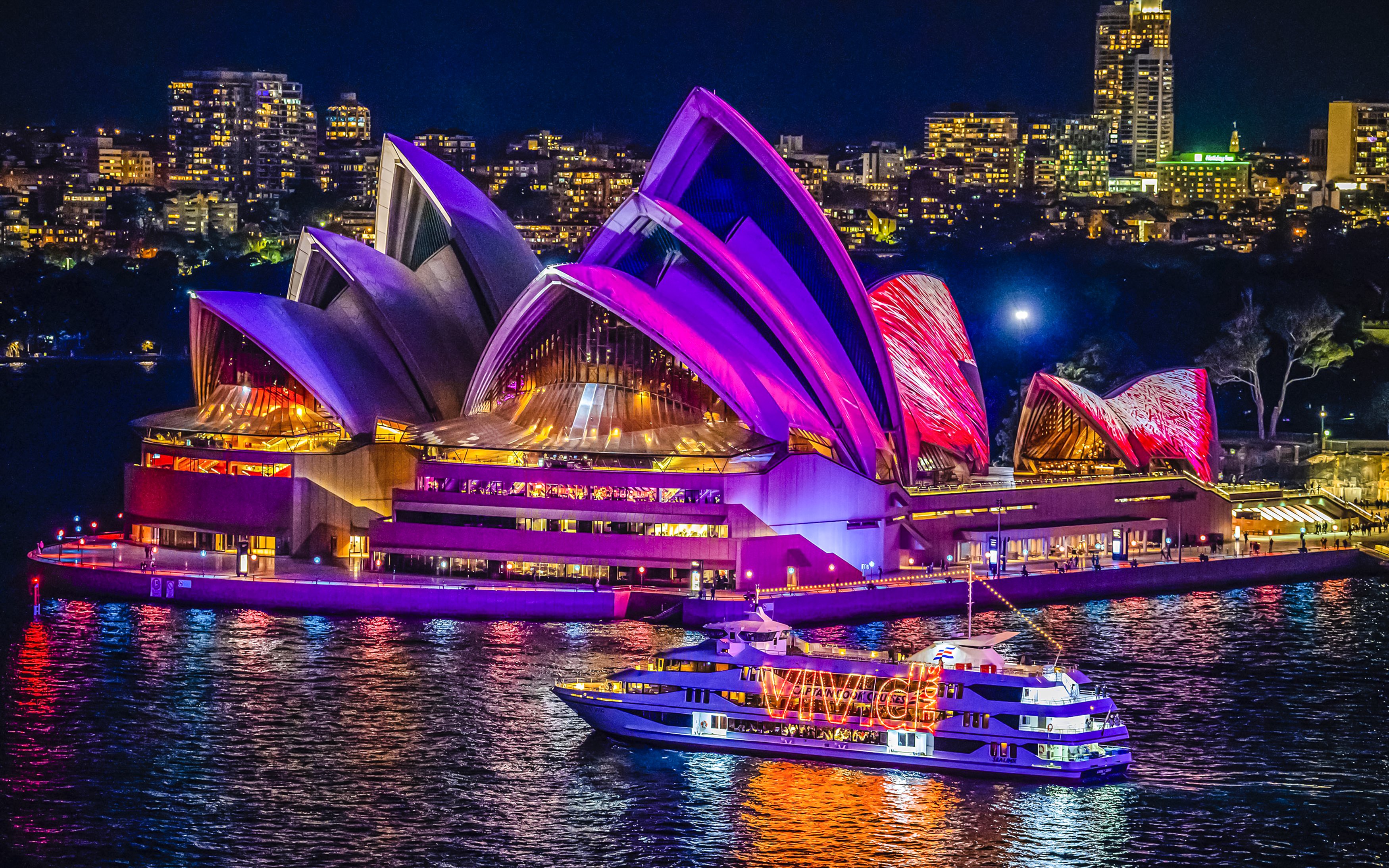 Sydney Opera House illuminated during harbour light show with cruise boat in foreground.