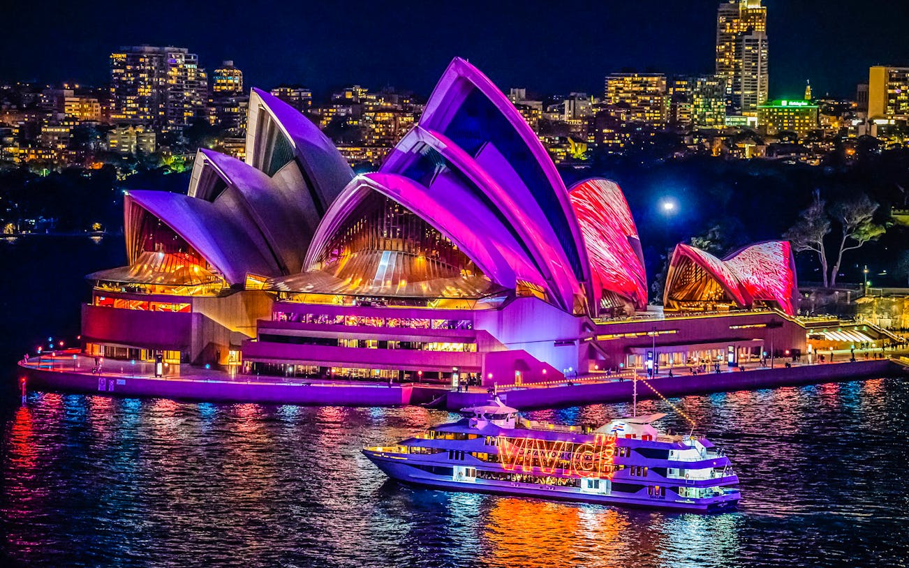 Sydney Opera House illuminated during harbour light show with cruise boat in foreground.