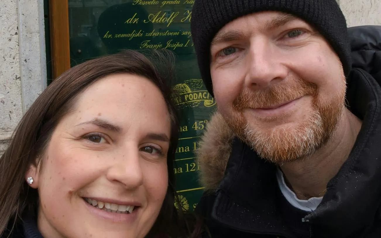 Two people smiling in front of a historic plaque during a self-guided city exploration in Zagreb.