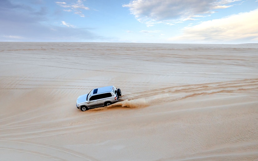 SUV driving on sand dunes during a dune bashing tour in Doha.