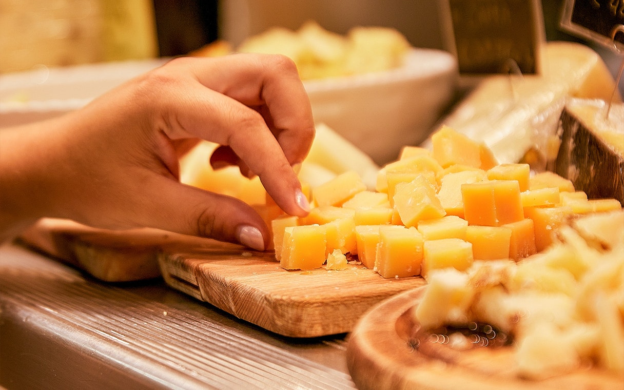 Tourist sampling cheese cubes at a market food tour.