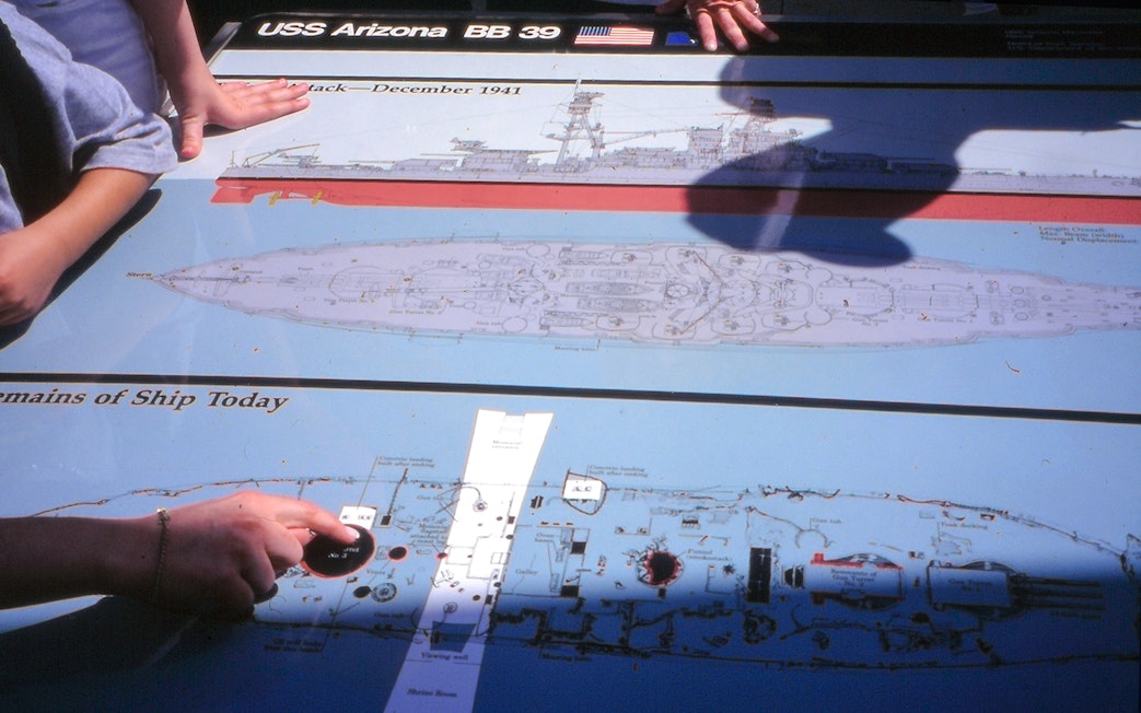 USS Arizona Memorial diagram with visitor hands pointing at ship layout, Pearl Harbor.