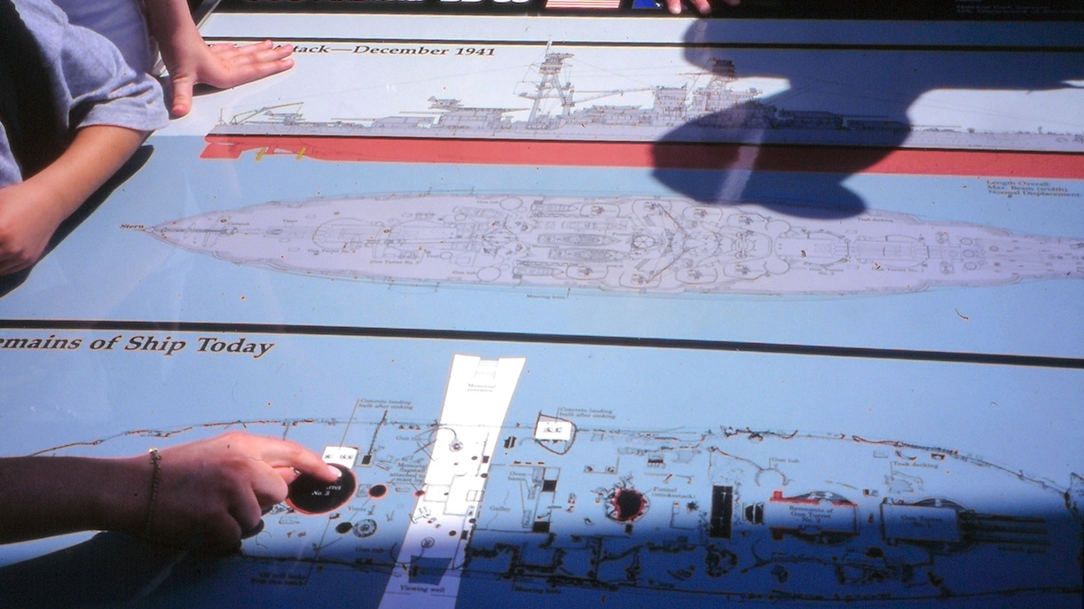 USS Arizona Memorial diagram with visitor hands pointing at ship layout, Pearl Harbor.