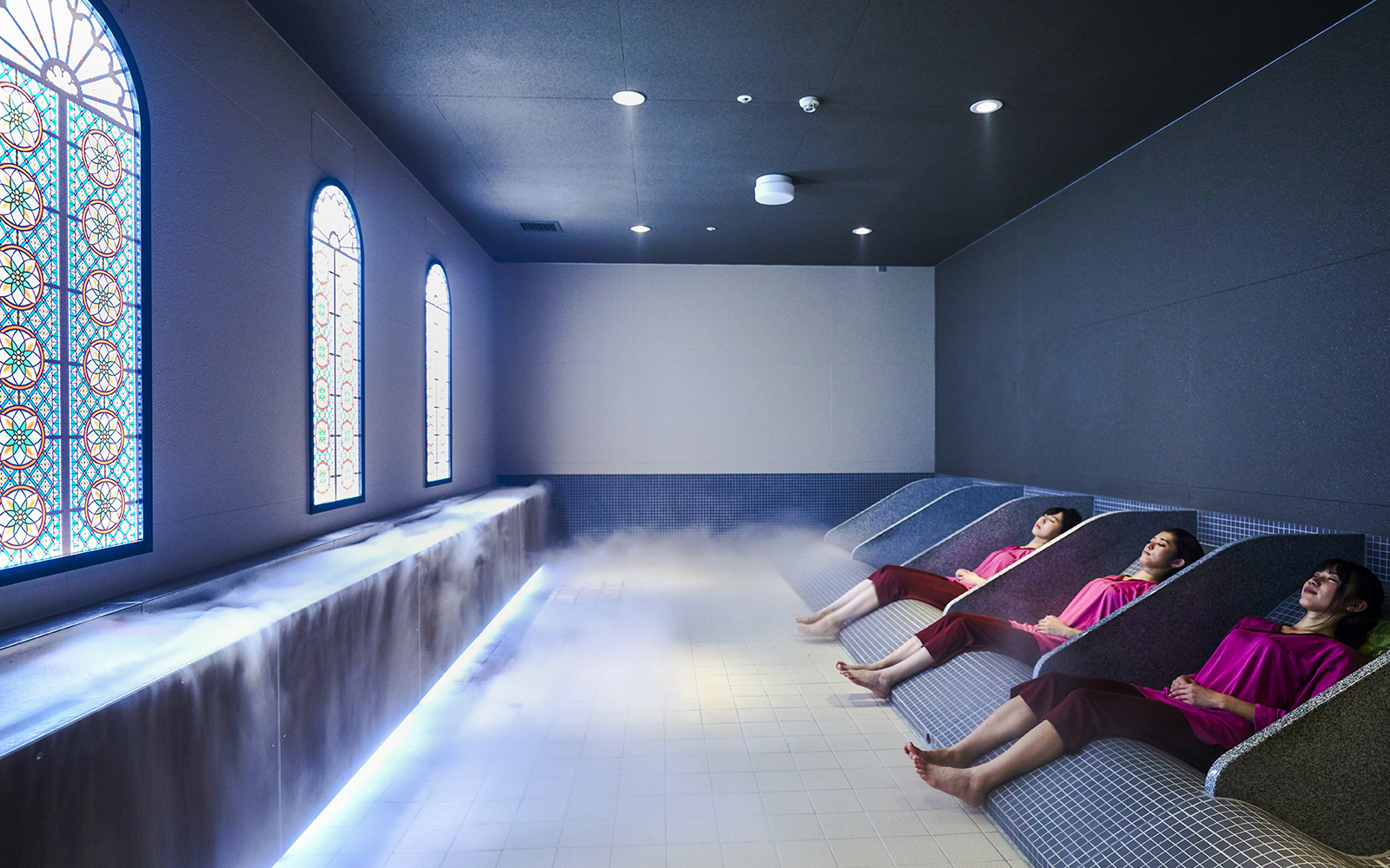 Visitors relaxing in Solaniwa Onsen baths with stained glass windows and ambient lighting.