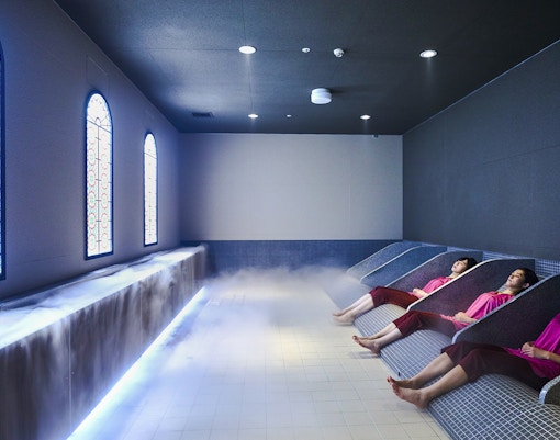 Visitors relaxing in Solaniwa Onsen baths with stained glass windows and ambient lighting.