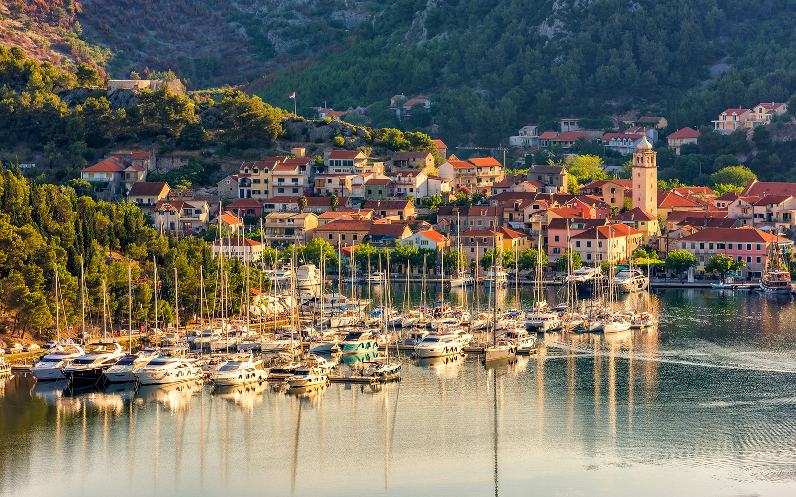 Sailboats docked in the harbor of Skradin, Croatia, with hillside houses and a church tower.