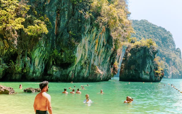 Tourists swimming in Krabi with limestone cliffs in the background.