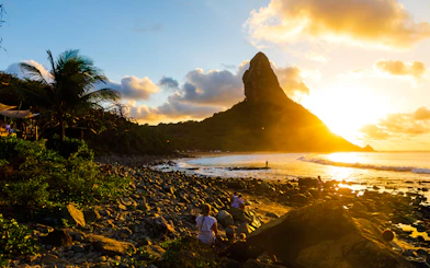 Sunset view of Morro do Pico with people on rocky beach, Fernando de Noronha, Brazil.