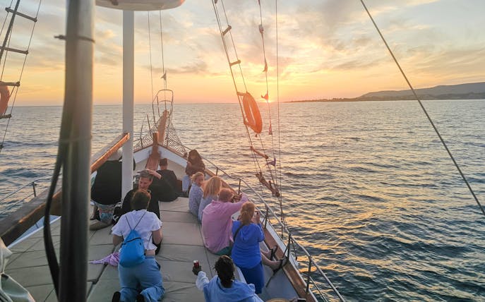 People enjoying a sunset cruise on a boat in Kefalonia, with a view of the sea and horizon.