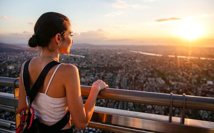 Girl on Taipei 101 observation deck at sunset, overlooking cityscape.