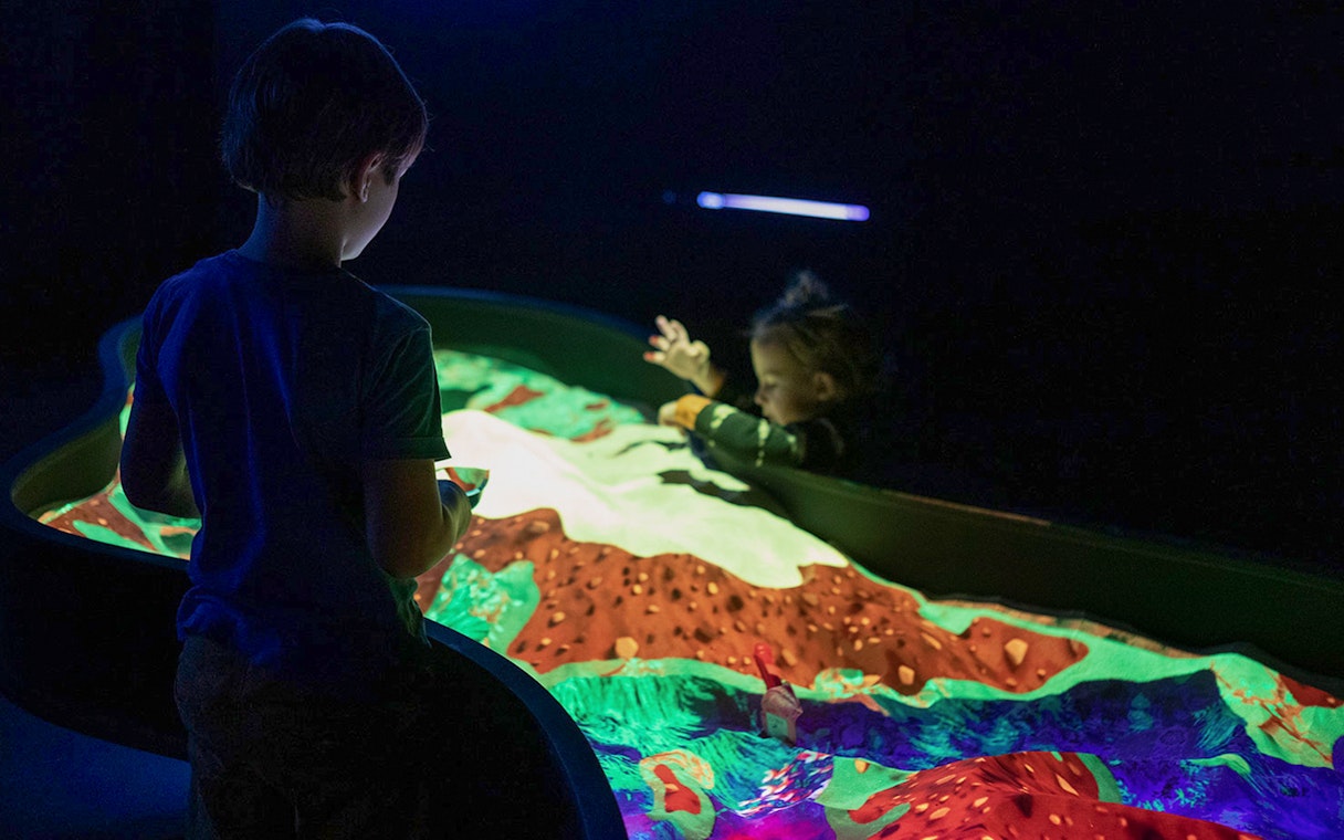 Children interacting with illuminated sand art at Lumia Gallery exhibition.