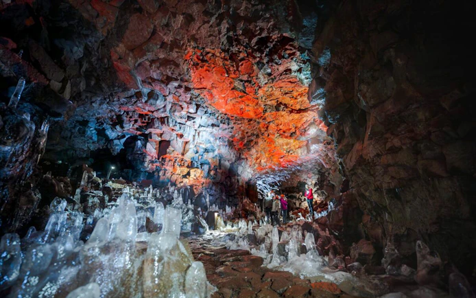 Guests exploring Raufarhólshellir Lava Tunnel with colorful rock formations and ice structures.