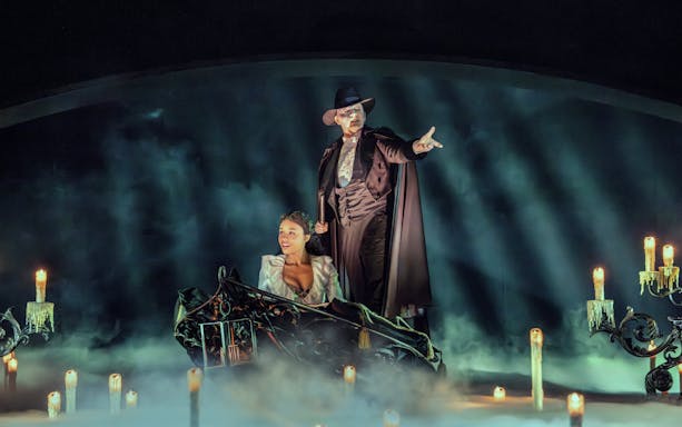 Phantom of the Opera scene with characters on a boat surrounded by candles and mist.