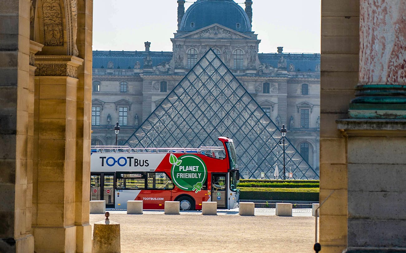 Hop On Hop Off bus in front of the Louvre Museum, Paris, offering city tours.