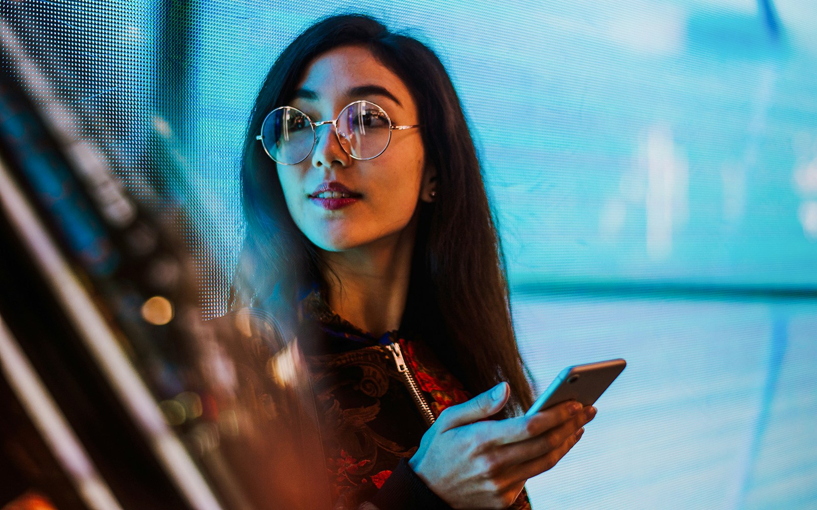 Woman holding a smartphone in front of a digital display.
