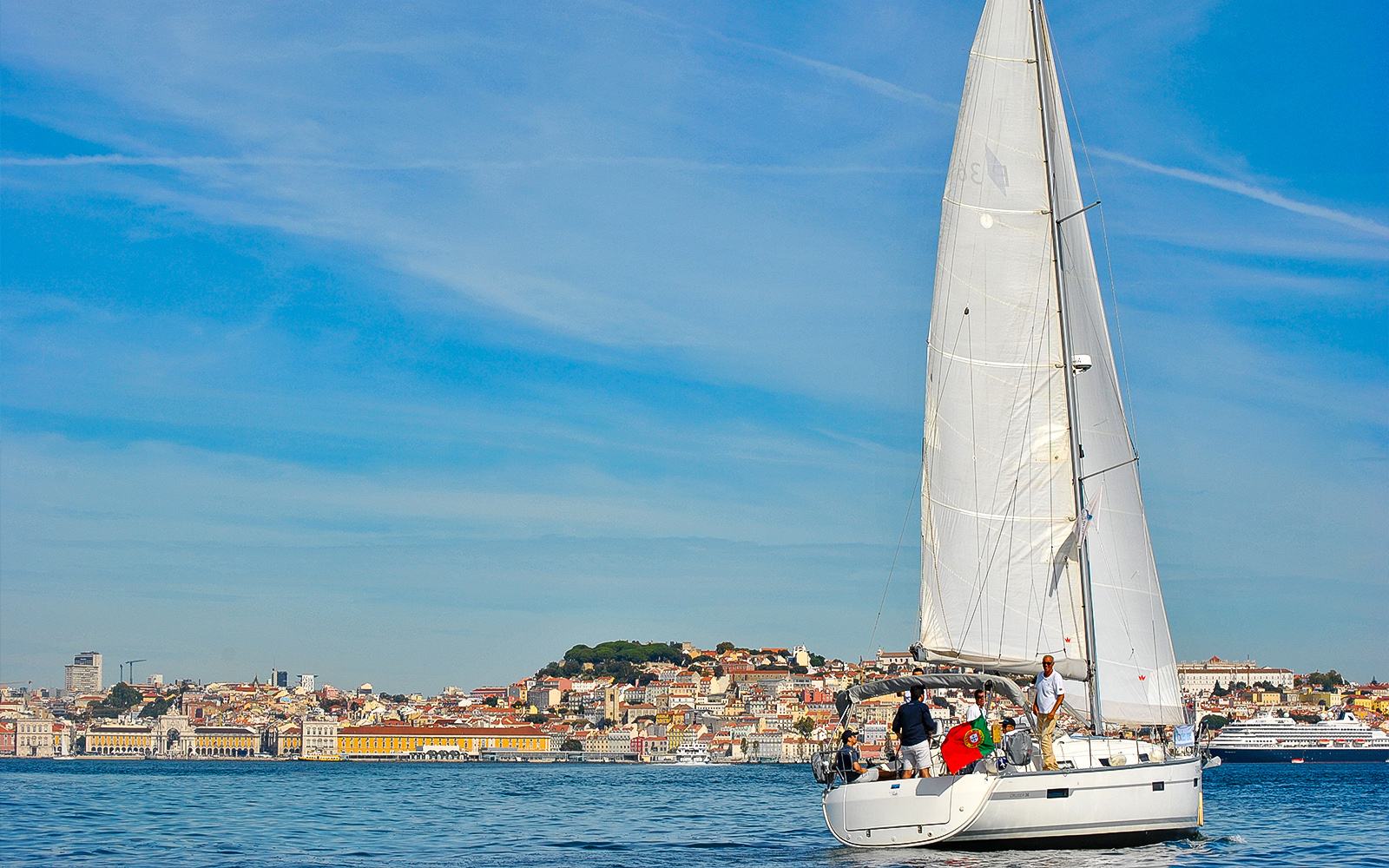 Sailboat on Tagus River with Lisbon cityscape in background.