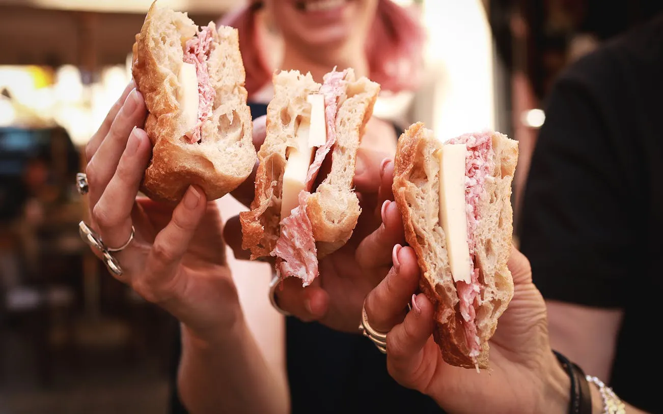 Sandwiches with cheese and cured meat held by people on Verona food tour.