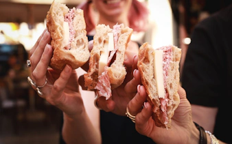 Sandwiches with cheese and cured meat held by people on Verona food tour.