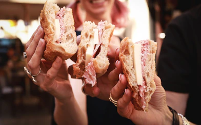 Sandwiches with cheese and cured meat held by people on Verona food tour.