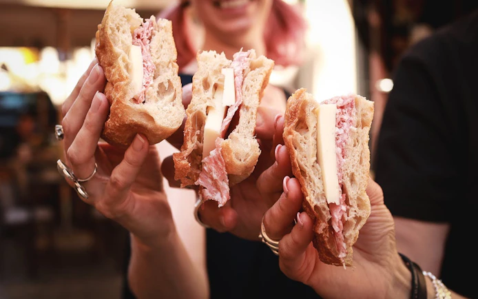 Sandwiches with cheese and cured meat held by people on Verona food tour.