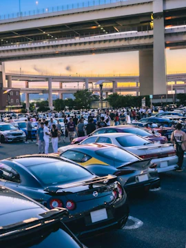 Car enthusiasts gather at Daikoku PA in Tokyo, showcasing a variety of vehicles under highway overpasses.