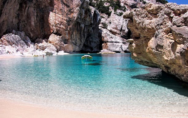 Boat anchored in clear waters near rocky cliffs on Costa di Baunei tour.