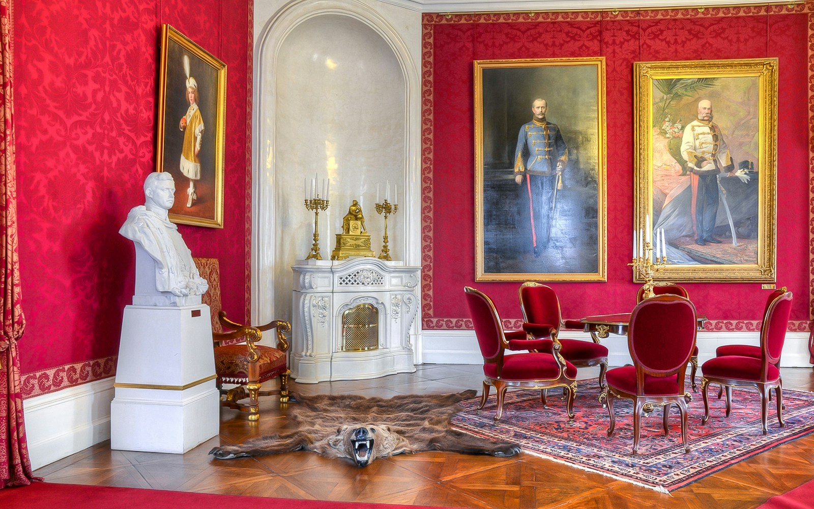 Interior of Royal Palace of Gödöllő with red walls, portraits, and ornate furniture.