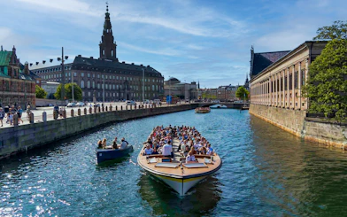Canal cruise boat with tourists in Copenhagen, passing historic buildings and a bridge.