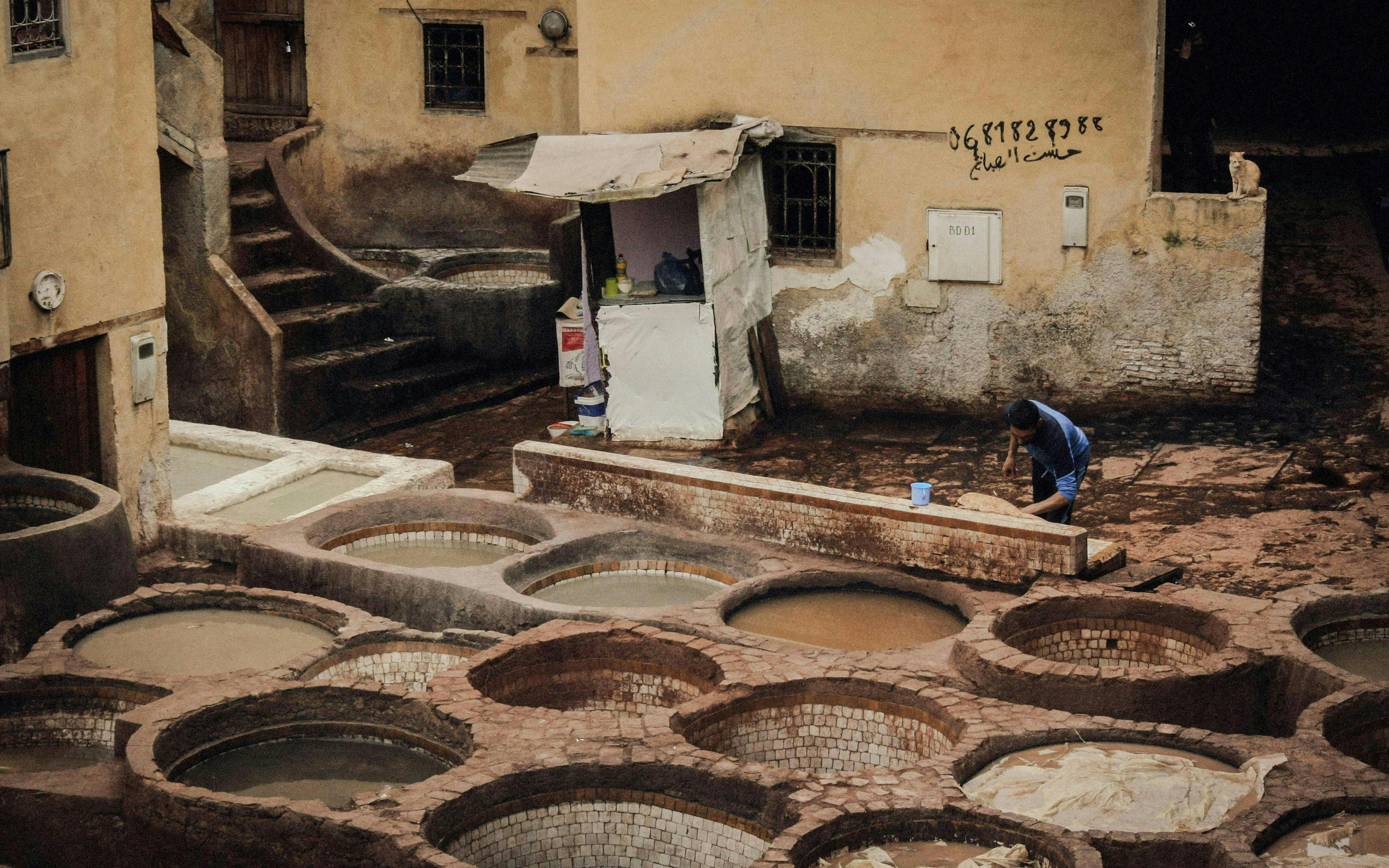 Tannery worker in Fes Old Medina preparing leather in traditional dyeing vats.