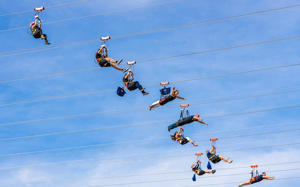 Zipliners soaring on Fly LINQ Zipline in Las Vegas against a clear sky.