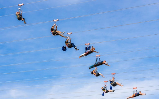 Zipliners soaring on Fly LINQ Zipline in Las Vegas against a clear sky.