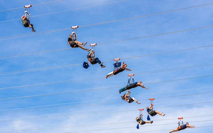 Zipliners soaring on Fly LINQ Zipline in Las Vegas against a clear sky.