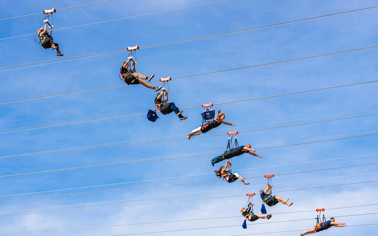 Zipliners soaring on Fly LINQ Zipline in Las Vegas against a clear sky.