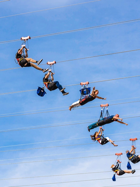Zipliners soaring on Fly LINQ Zipline in Las Vegas against a clear sky.