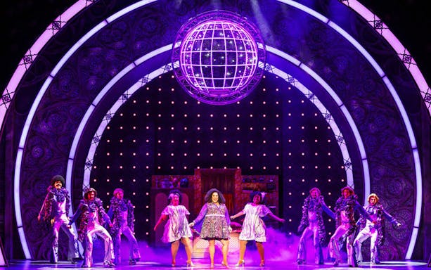 Performers on stage in a vibrant "Sister Act" musical scene with disco ball.